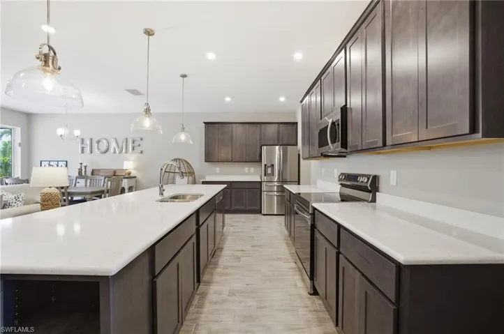 Modern kitchen featuring an expansive center island with an undermount sink, white countertops, dark wood cabinetry, and stainless steel appliances