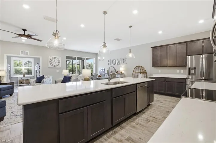 Open-concept kitchen featuring an oversized island with double sink, stainless steel appliances, dark wood cabinetry, white countertops, and wood-finish flooring