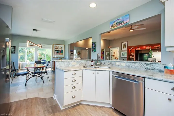 Kitchen with dishwasher, white cabinets, sink, light stone counters, and kitchen peninsula
