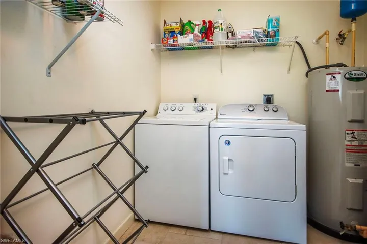 Laundry area featuring light tile patterned floors, electric water heater, and washing machine and dryer
