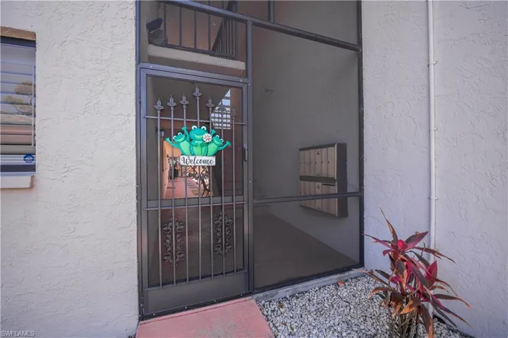 Screened entryway featuring a decorative metal security door, textured stucco exterior, and an adjacent window with horizontal blinds