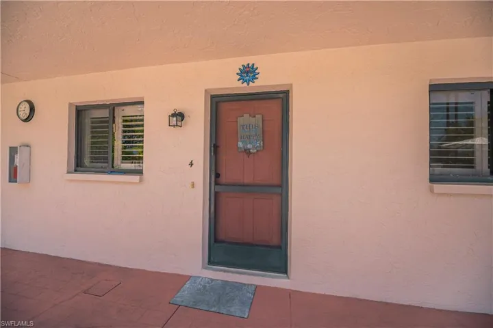 Entryway featuring a screened door with a security lock, a wall-mounted outdoor light fixture, and two windows with horizontal blinds