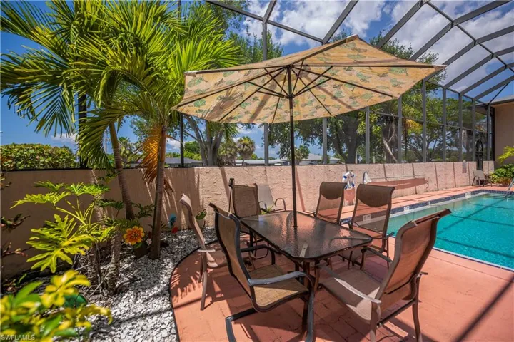 Screened outdoor living area featuring a rectangular swimming pool with a tile border, a textured privacy wall, and mature palm trees