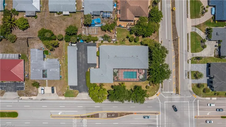 Aerial perspective of a property featuring a rectangular pool, mature trees, and direct road frontage