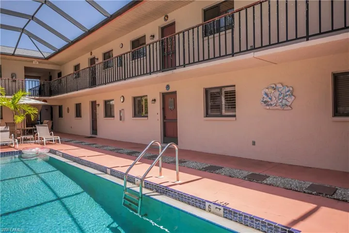 Screened-in courtyard pool area featuring a clear blue swimming pool with steps, a terracotta-colored pool deck, and a two-story building with multiple entry doors and a second-level balcony with black railings