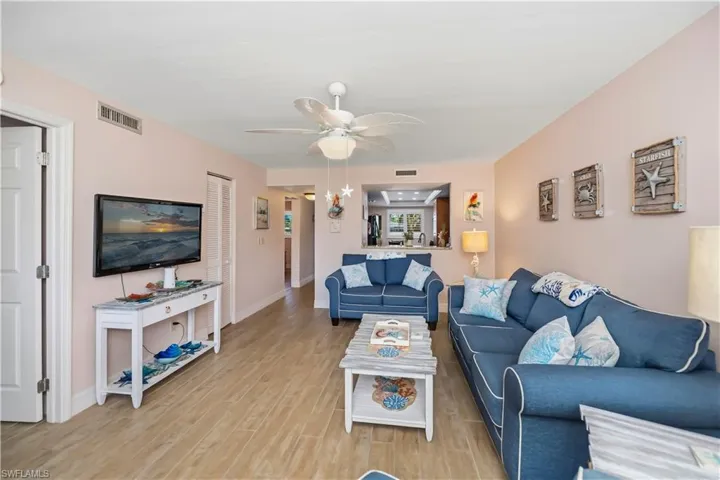 Open living space featuring wood-finish flooring, a ceiling fan with light fixture, and a pass-through opening to an adjacent room