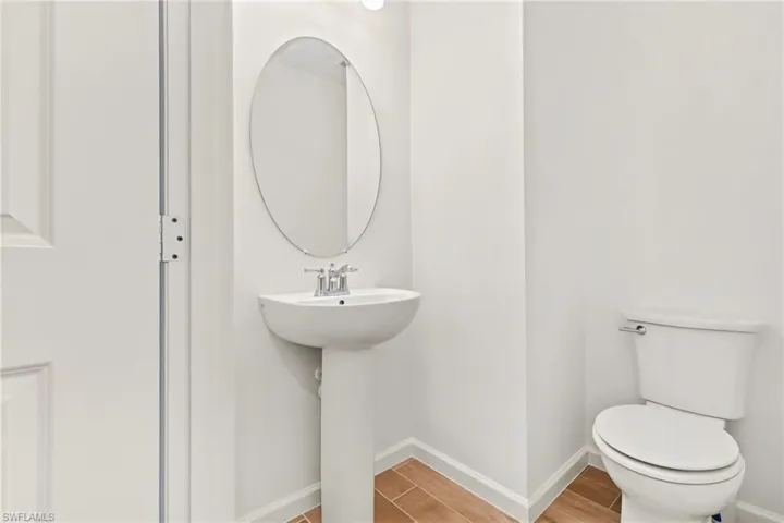 Pedestal sink with chrome faucet, oval mirror, and wood-finish flooring