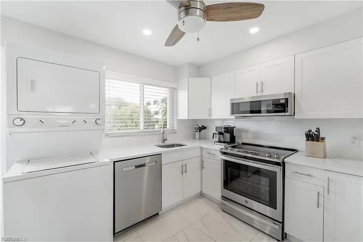 Kitchen with stacked washer and clothes dryer, appliances with stainless steel finishes, white cabinets, ceiling fan, and tasteful backsplash