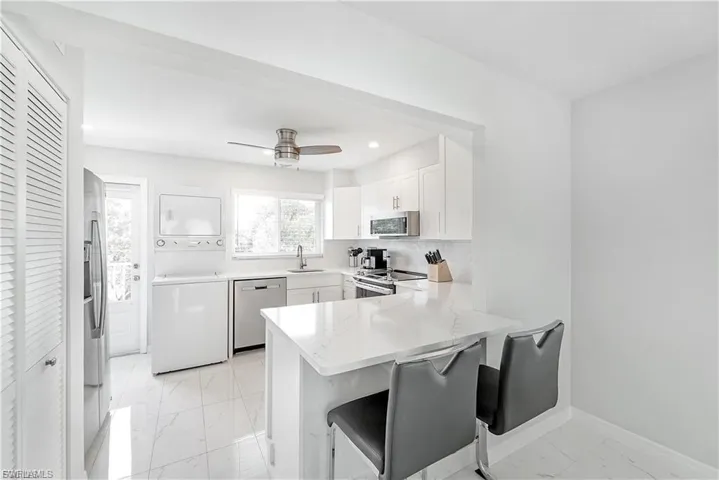 Kitchen featuring stacked washer / drying machine, light marble finish floors, stainless steel appliances, a peninsula, and white cabinetry