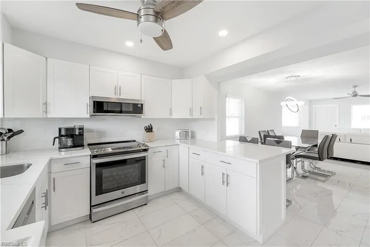 Kitchen featuring a ceiling fan, appliances with stainless steel finishes, a peninsula, light marble finish floors, and white cabinetry