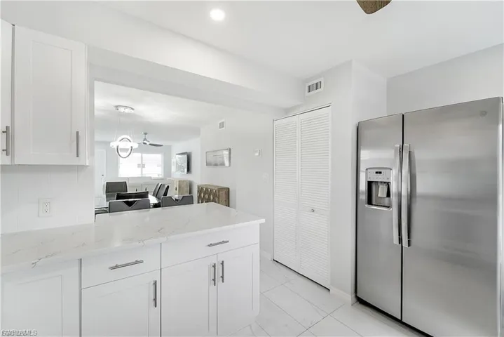 Kitchen with stainless steel fridge, white cabinetry, light stone countertops, a peninsula, and recessed lighting