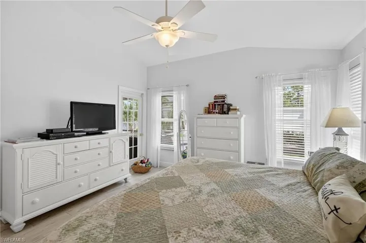 Bright interior room featuring a vaulted ceiling with a ceiling fan, light wood-finish flooring, and multiple windows with blinds