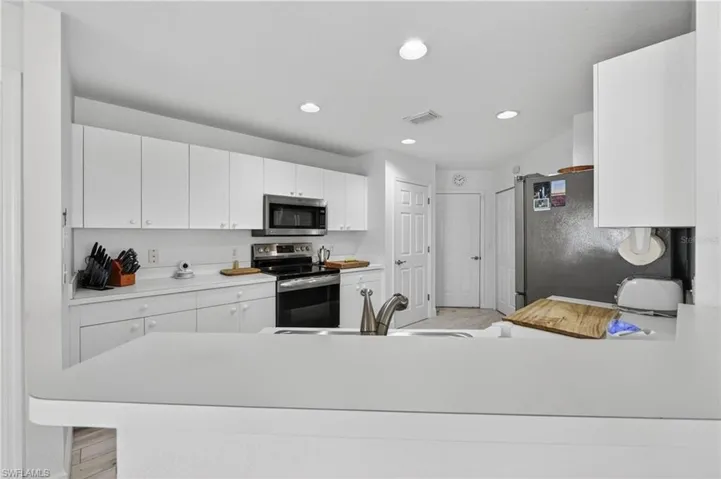 Kitchen featuring white cabinetry, light-toned countertops, stainless steel appliances, a kitchen island with an integrated sink, and recessed lighting