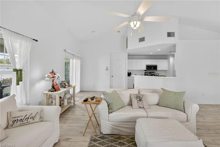 Open-concept living area with vaulted ceilings, wood-finish flooring, a ceiling fan, and sliding glass doors to the exterior