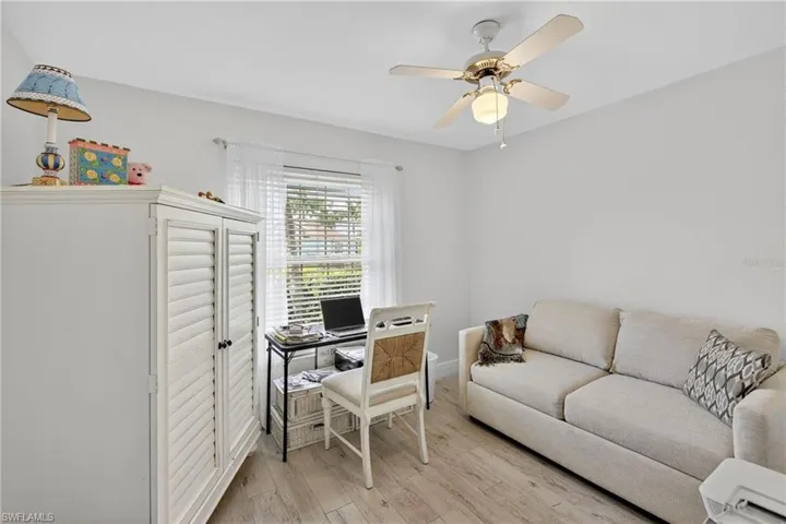 Light-filled room featuring wood-finish flooring, a ceiling fan with integrated lighting, and a window dressed with white blinds and sheer curtains