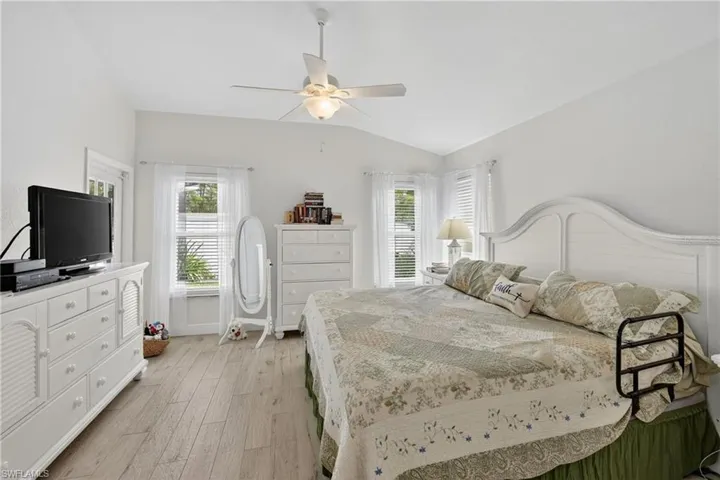 Spacious room featuring vaulted ceilings, light wood-finish flooring, multiple windows with blinds, and a ceiling fan with integrated lighting