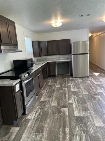 Kitchen with stainless steel appliances, under cabinet range hood, dark brown cabinetry, and a textured ceiling