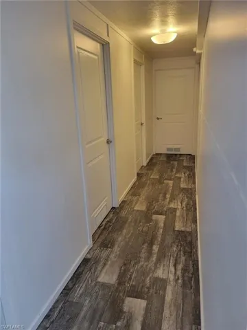 Hall with dark wood-style flooring, visible vents, baseboards, and a textured ceiling
