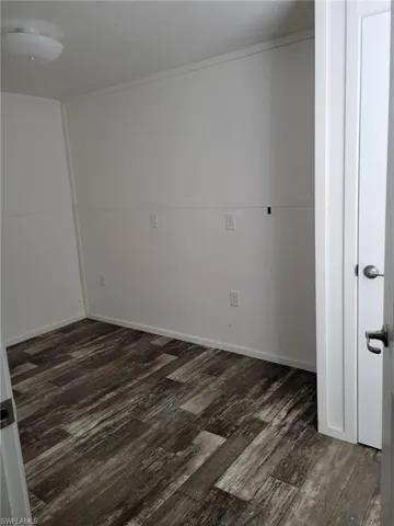 Empty room with dark wood-style flooring, baseboards, and crown molding