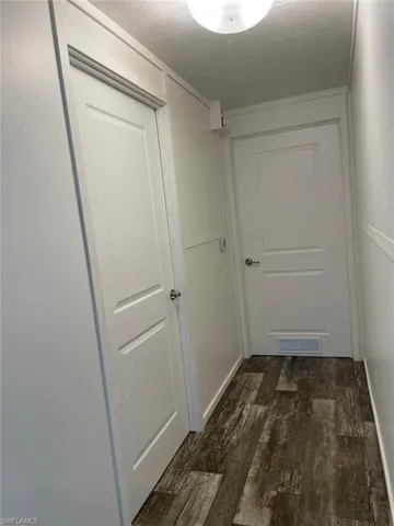 Hallway with a textured ceiling, dark wood-style flooring, and visible vents