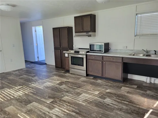 Kitchen with a sink, appliances with stainless steel finishes, dark brown cabinetry, under cabinet range hood, and dark wood-type flooring