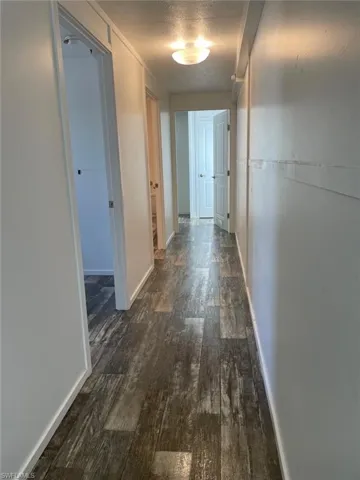 Corridor with dark wood-type flooring, a textured ceiling, and baseboards