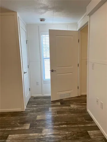 Entrance foyer with dark wood-style flooring, visible vents, baseboards, and a textured ceiling