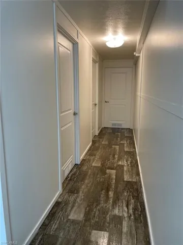 Hall with a textured ceiling, baseboards, dark wood-style floors, and visible vents