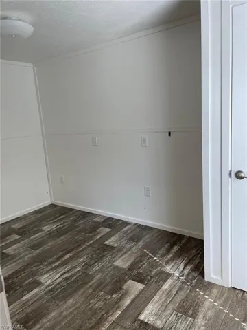 Unfurnished room with a textured ceiling, baseboards, and dark wood finished floors