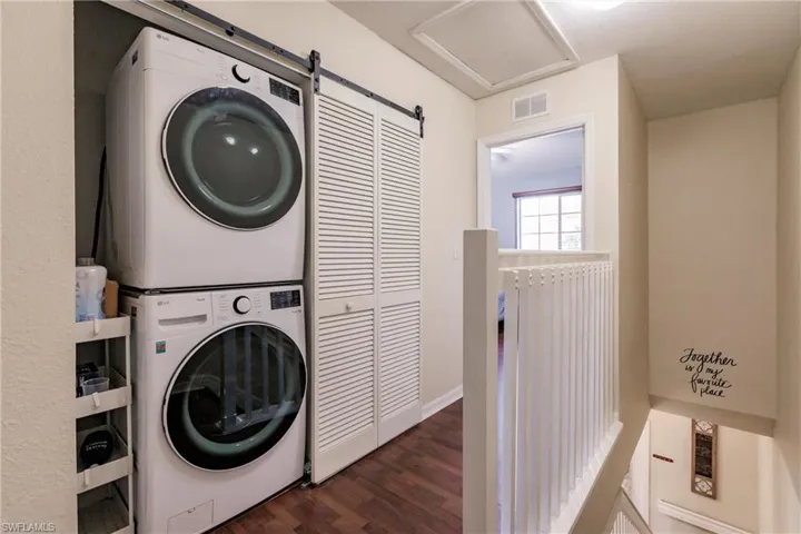 Clothes washing area with stacked washer and clothes dryer, a barn door, and dark hardwood / wood-style flooring