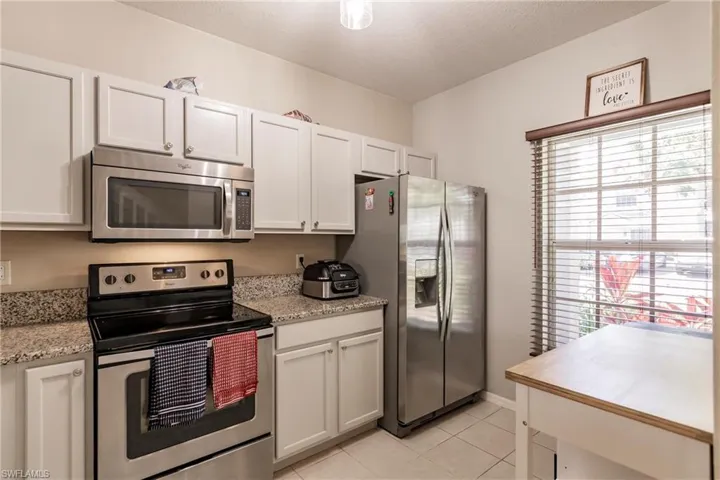 Kitchen featuring stainless steel appliances, light stone counters, white cabinetry, and light tile floors