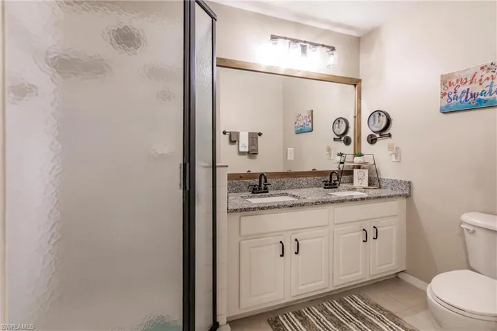 Bathroom featuring double vanity, walk in shower, toilet, and tile floors