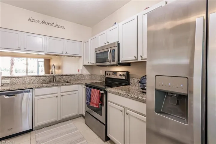 Kitchen featuring stainless steel appliances, light tile flooring, light stone counters, sink, and white cabinetry