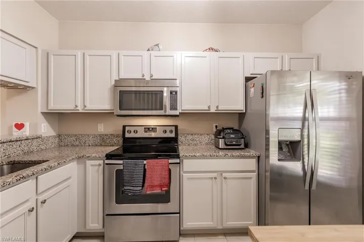 Kitchen featuring light stone countertops, white cabinetry, and appliances with stainless steel finishes