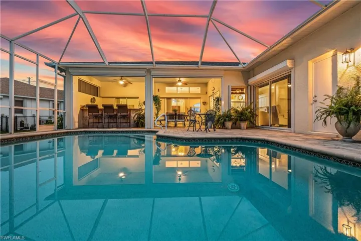 Pool at dusk featuring a patio, ceiling fan, and glass enclosure