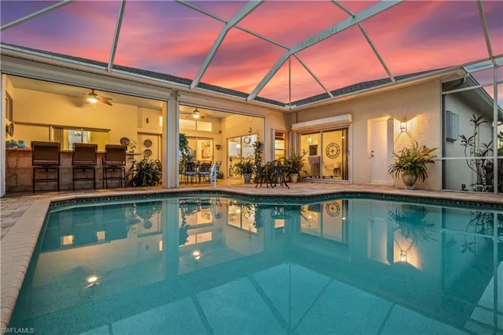 Pool at dusk with glass enclosure, a bar, a patio area, and ceiling fan