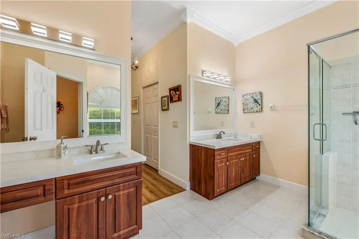 Bathroom featuring dual vanity, a shower with door, crown molding, and wood-type flooring