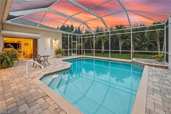 Pool at dusk featuring a patio and glass enclosure