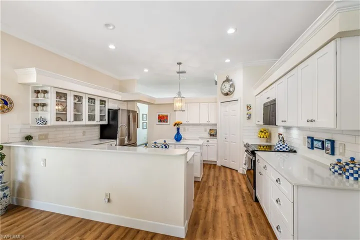 Kitchen with white cabinetry, hanging light fixtures, decorative backsplash, light wood-type flooring, and appliances with stainless steel finishes