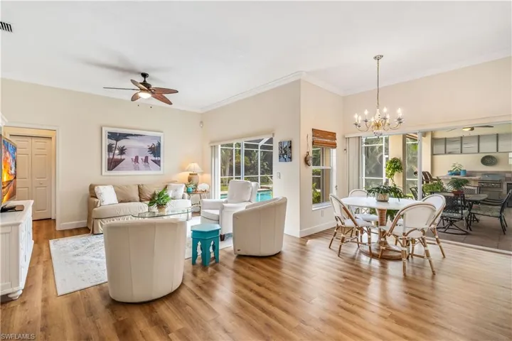 Living room with wood-type flooring, ceiling fan with notable chandelier, and crown molding