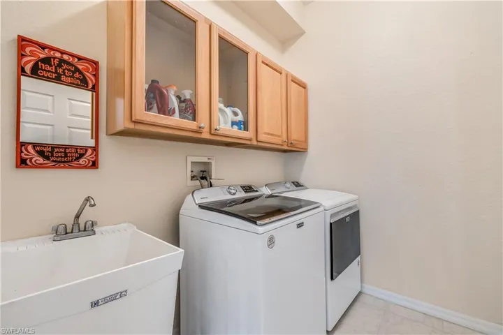 Laundry room with sink, cabinets, light tile patterned floors, and washing machine and clothes dryer