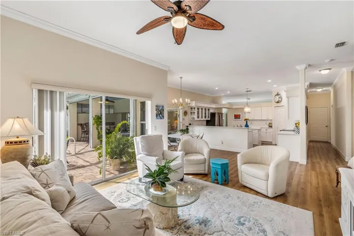 Living room with ceiling fan with notable chandelier, light hardwood / wood-style flooring, and ornamental molding