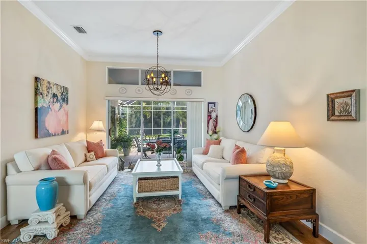 Living room with dark hardwood / wood-style flooring, ornamental molding, and an inviting chandelier