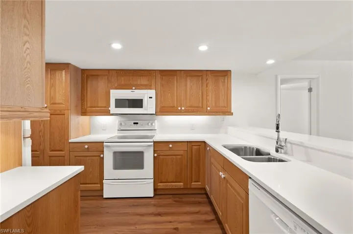 Kitchen with white appliances, recessed lighting, dark wood-type flooring, and brown cabinetry