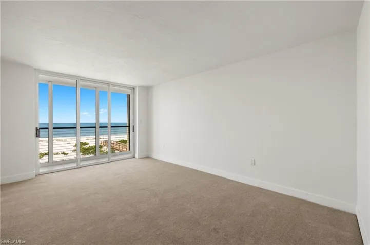 Carpeted empty room with a wall of windows, view of water and beach, and a textured ceiling