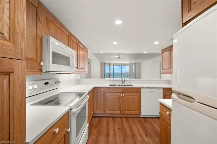 Kitchen featuring white appliances, light wood finished floors, light countertops, recessed lighting, and brown cabinetry