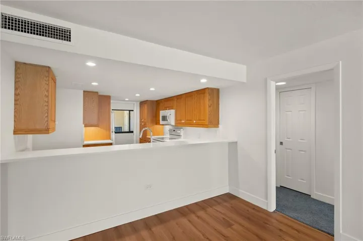 Kitchen featuring recessed lighting, dark wood-style flooring, brown cabinets, light countertops, and white appliances