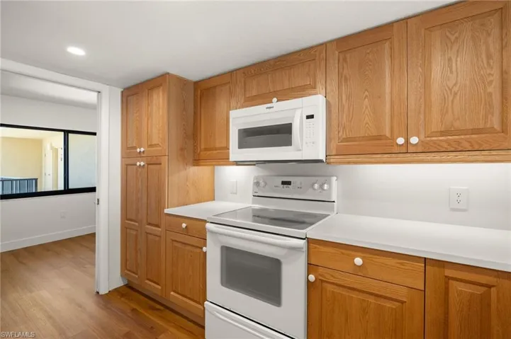 Kitchen featuring white appliances, light wood-style floors, light countertops, recessed lighting, and brown cabinetry