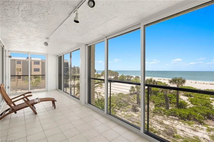 Unfurnished sunroom featuring expansive windows, view of water and beach, tile patterned flooring, track lighting, and a textured ceiling