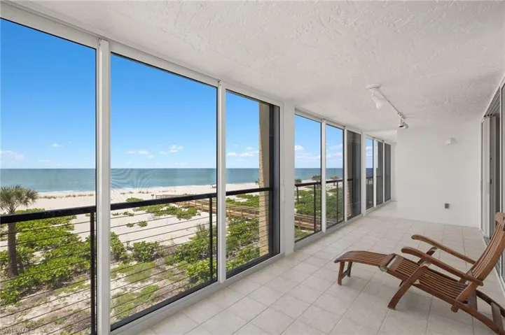 Sunroom with floor to ceiling windows, view of water and beach, rail lighting, a textured ceiling, and tile patterned floors